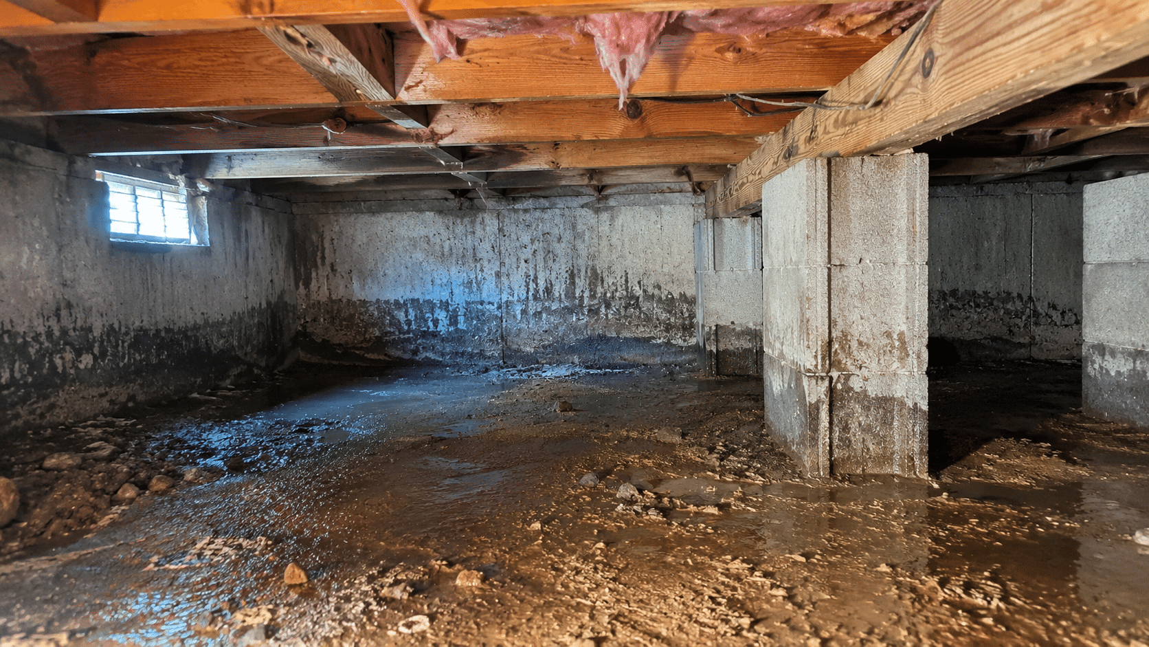 Damp residential crawlspace with visible moisture conditions and wet soil beneath wood framing